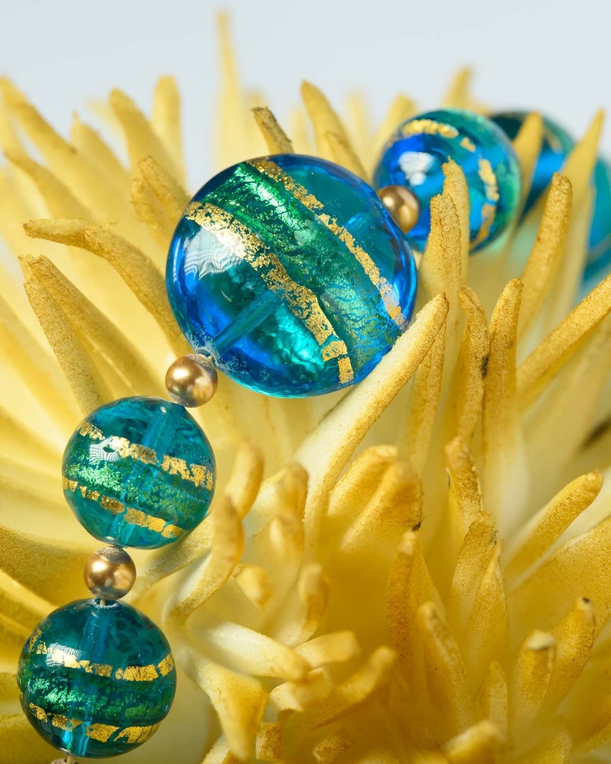 Close-up of a Murano necklace with vibrant blue and green beads featuring gold accents, displayed on a yellow decorative piece